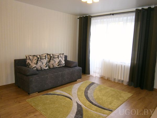 Диван с узорчатыми подушками, абстрактный ковер и вертикальные обои создают чистую и стильную атмосферу.