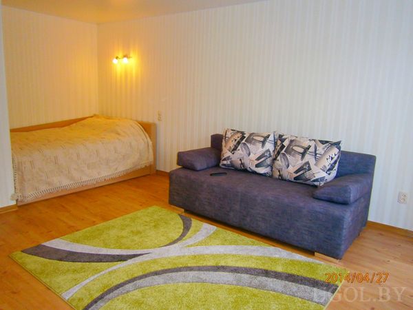 Кровать и диван с принтом «Эйфелева башня» в одном пространстве, дополненные зелёным ковром и точечным освещением.