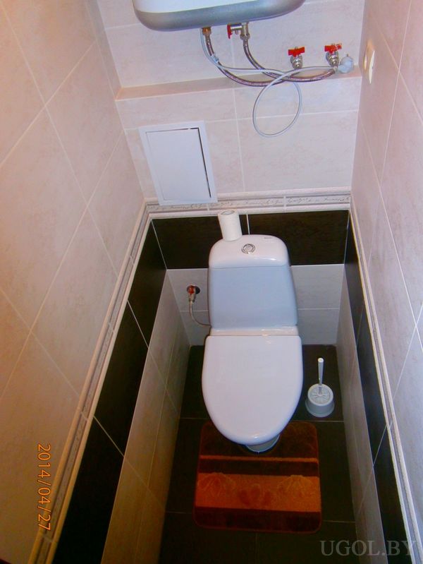 Узкое помещение с унитазом, водонагревателем и контрастной плиткой, подчёркивающее рациональное использование пространства.