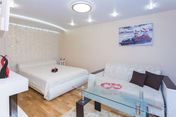 Современная комната с белой кроватью, диваном, стеклянным столиком и стеной с круговым узором.