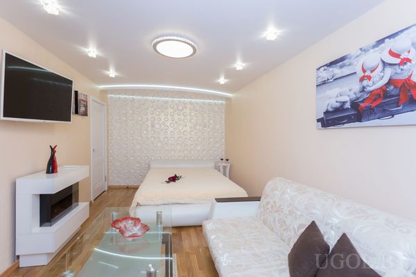 Минималистичная спальня с белой кроватью, диваном, стеклянным столиком и декоративной панелью с кругами.