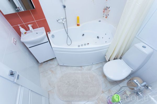 Современная ванная с угловой ванной с гидромассажем, унитазом, раковиной и красной плиткой у зеркала.