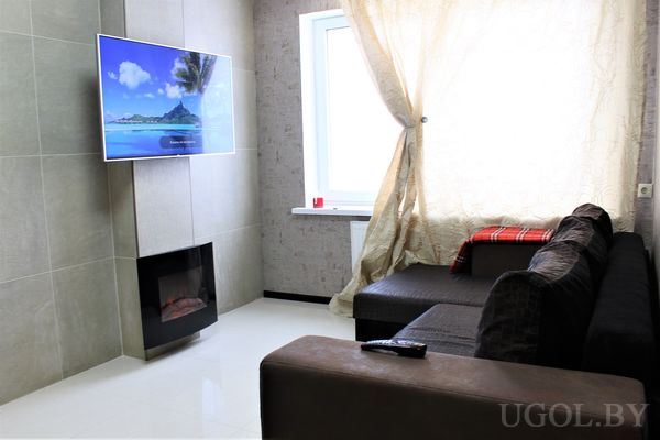 Комната с диваном, телевизором, камином, пледом, тюлем и светлой плиткой.