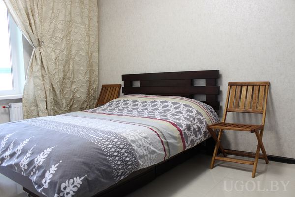 Интерьер с кроватью, покрывалом, стульями, шторами, светлой плиткой и нейтральной отделкой.