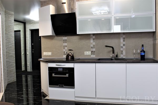 Рабочая зона с плитой, вытяжкой, раковиной, вином, бокалами и глянцевым полом.