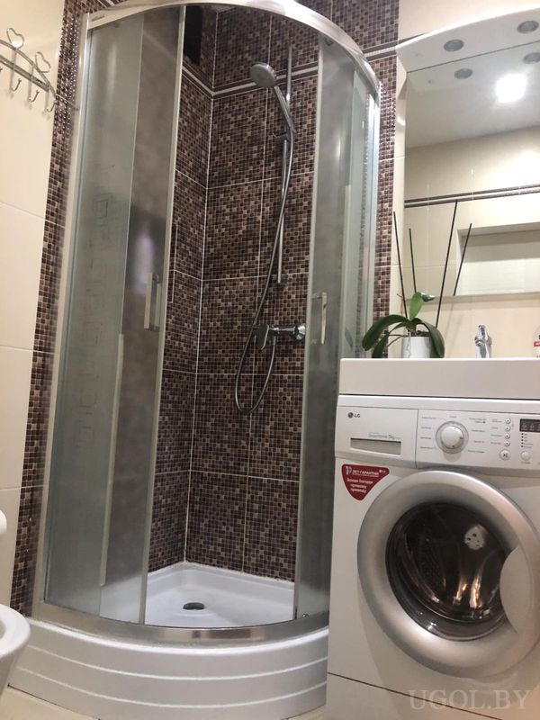 Современная ванная с душевой кабиной, стиральной машиной и полкой с орхидеей.