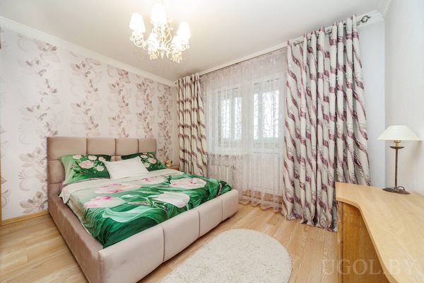 Интерьер с кроватью, цветочными шторами, люстрой и деревянным столом у стены.