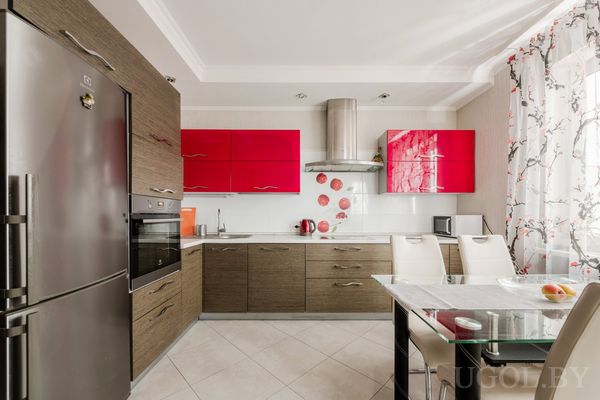 Интерьер с красными шкафами, встроенной техникой, стеклянным столом и фартуком с томатным узором.