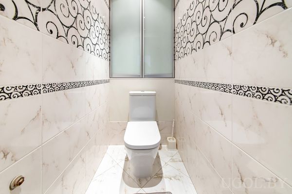 Узкое помещение с унитазом, мраморной плиткой и чёрным бордюром с орнаментом.