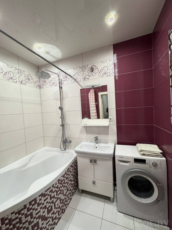 Комната с ванной, душем, умывальником, зеркалом, машиной, бордовой плиткой и декоративной вставкой.