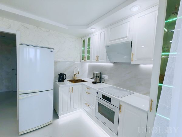 Интерьер с белыми шкафами, мраморным фартуком, техникой, золотым смесителем и встроенной подсветкой.