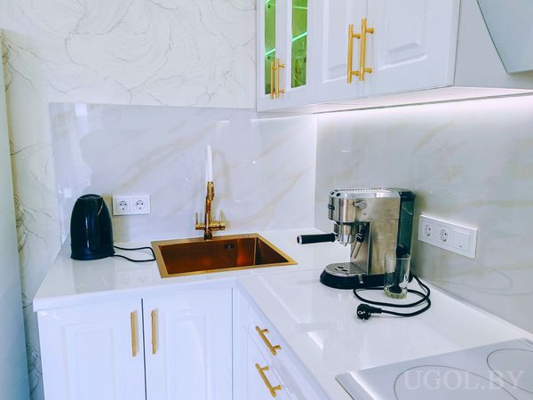 Рабочая поверхность с медной мойкой, белыми шкафами, стеклянными фасадами и техникой на фоне мрамора.