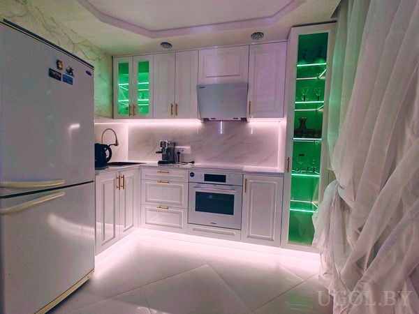 Интерьер с белыми шкафами, встроенной техникой, зелёной подсветкой, белым холодильником и глянцевым полом.