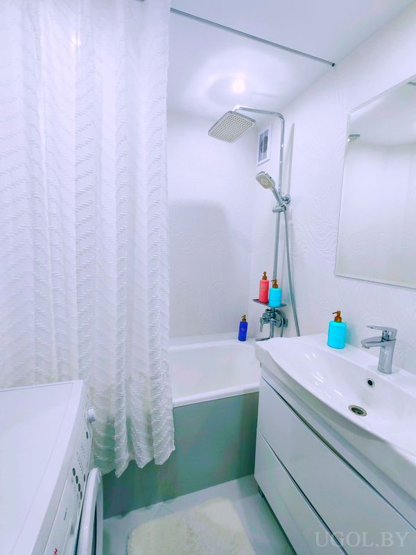 Комната с ванной, умывальником, машиной, белыми стенами и яркими дозаторами на бортиках.