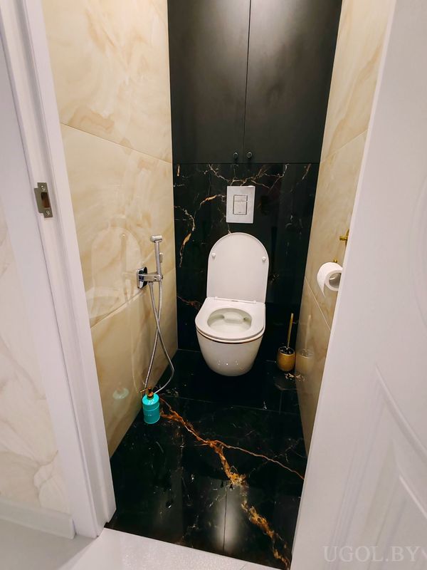 Интерьер с унитазом, чёрной плиткой с золотыми прожилками, шкафом, ёршиком и освежителем.