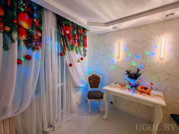 Зона с белым столом, ёлкой, фруктами, гирляндами и шторами с праздничным орнаментом.