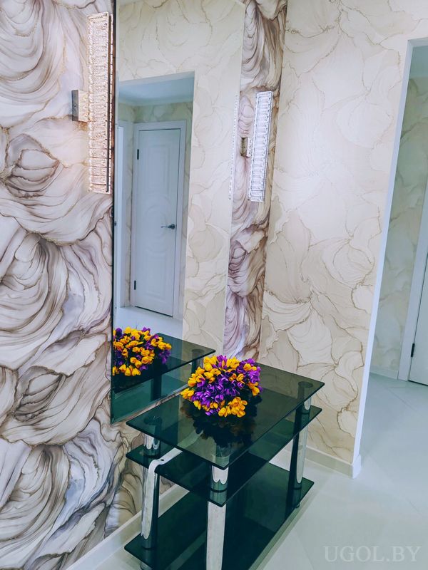 Зона с зеркалом, стеклянной консолью, цветами, светильниками и мраморными обоями.