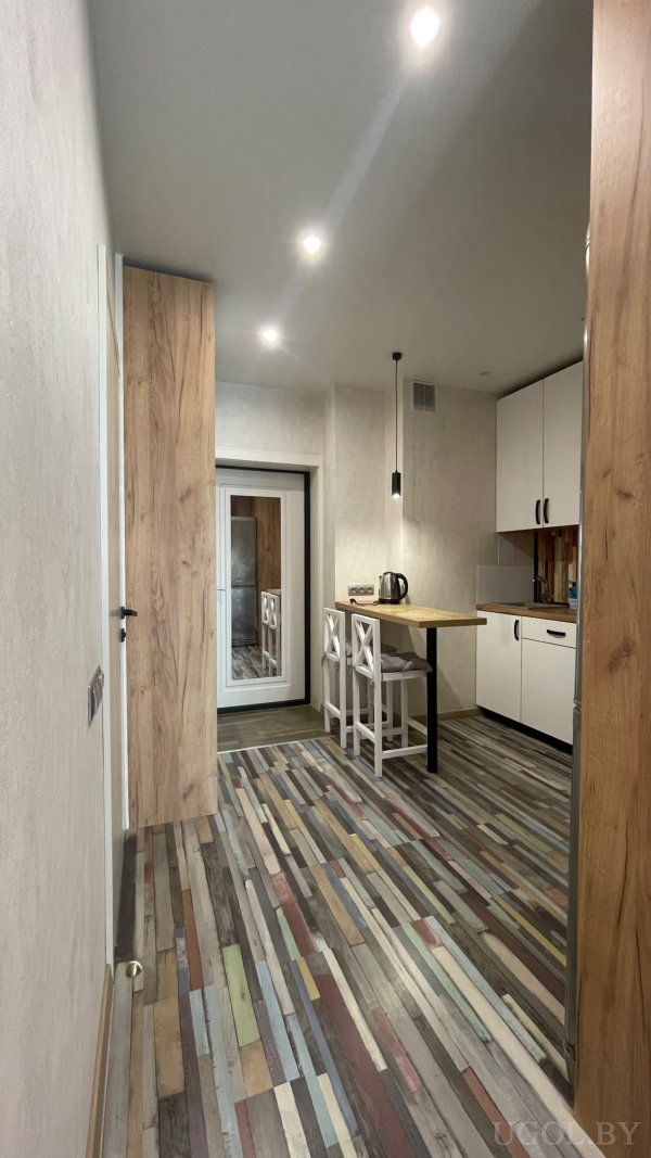 Небольшой стол с двумя белыми стульями, белые фасады с чёрными ручками, вертикальный полосатый фартук и зеркало на двери.