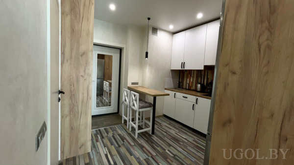 Белые шкафы с чёрными ручками, деревянная столешница, встроенные духовой шкаф и микроволновка, пёстрый вертикальный фартук и два высоких стула.