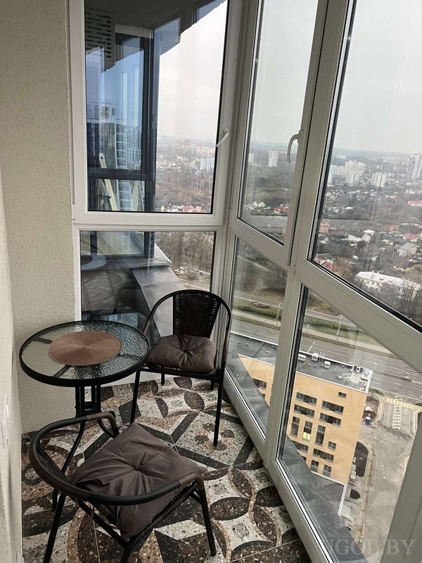 Балкон с плиткой в коричневых тонах, плетёной мебелью и видом на дороги, дома и зелёные зоны.