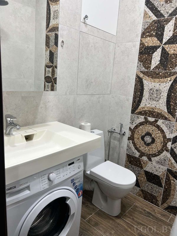 Компактная ванная с умывальником над машинкой, туалетом, серой плиткой и декоративным фартуком.