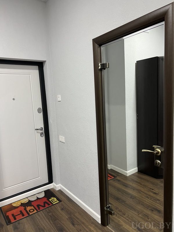 Входная зона с белой дверью, ковриком «HOME», стеклянной дверью в комнату и тёмным ламинатом.