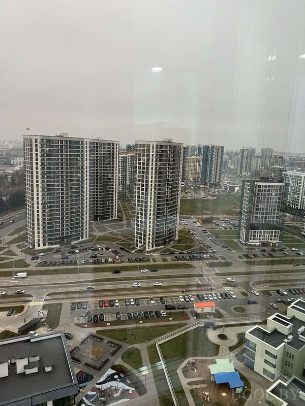 Городской вид с высоты на высотки, парковку, детскую площадку и зелёные зоны между домами.