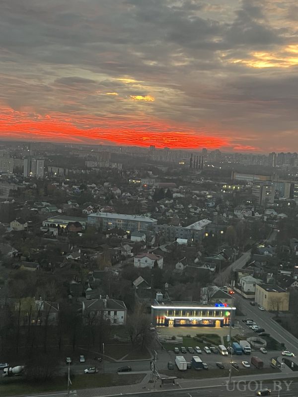 Городской пейзаж с закатным небом, жилыми домами, дорогами и ярким светом на горизонте.