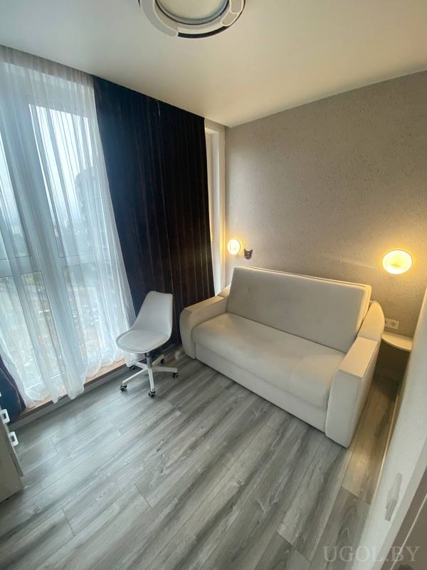 Минималистичный интерьер с белым диваном, настенными светильниками, рабочим креслом и серыми шторами.