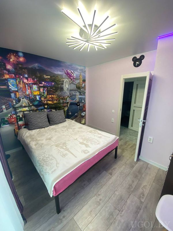 Комната с кроватью, фреской с огнями и машинками, потолочным светильником и декором в виде головы Микки Мауса.