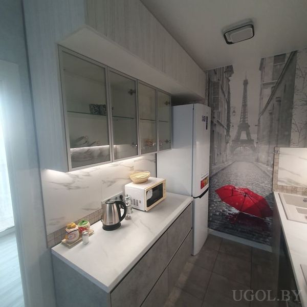 Кухонная зона с белыми фасадами, техникой и фреской с Эйфелевой башней и красным зонтом.