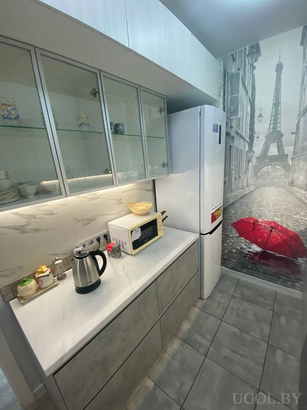 Интерьер с белыми фасадами, стеклянными шкафами, фреской Парижа и ярким акцентом на фоне серой плитки.