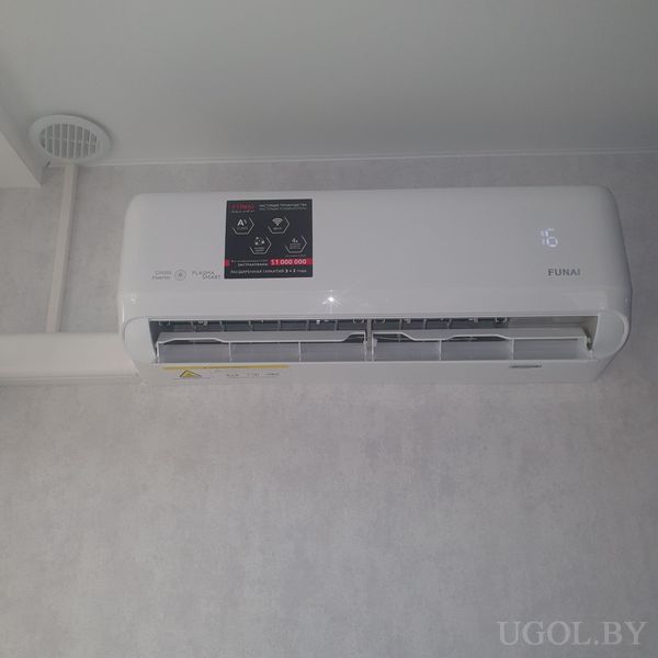 Настенный кондиционер с цифровым индикатором, наклейкой с характеристиками и открытыми жалюзи.