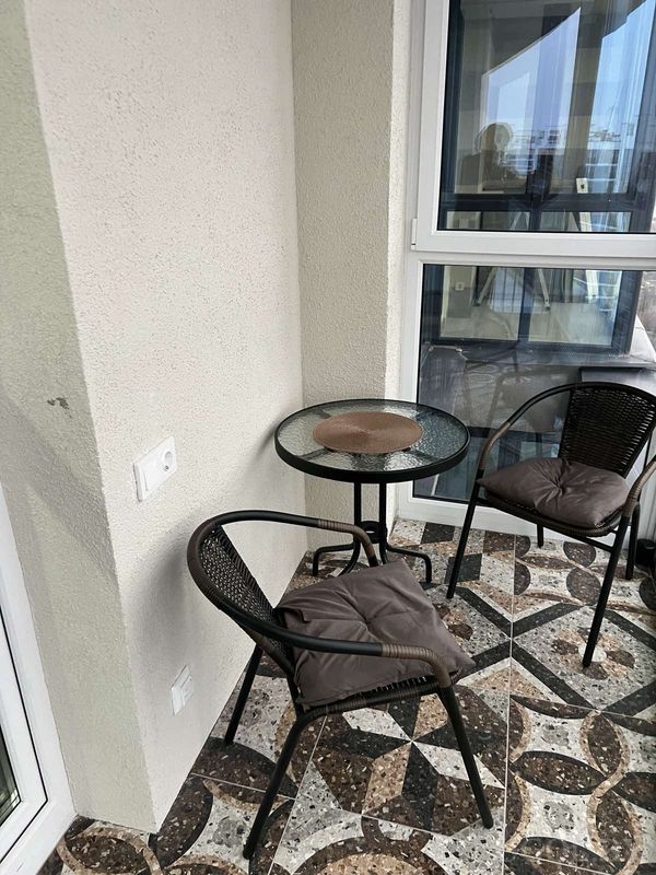 Уютный балкон с двумя креслами, стеклянным столиком, плиткой с узором и отражением интерьера в окне.