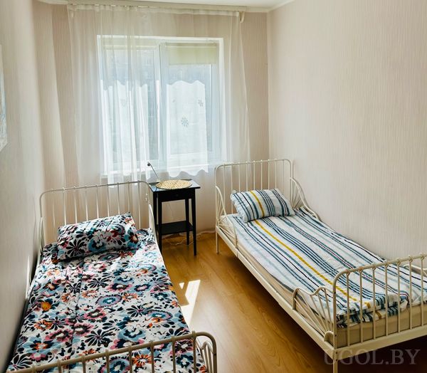 Спальня с двумя односпальными кроватями, тумбой с лампой, корзиной и текстилем с цветочным и полосатым узором.