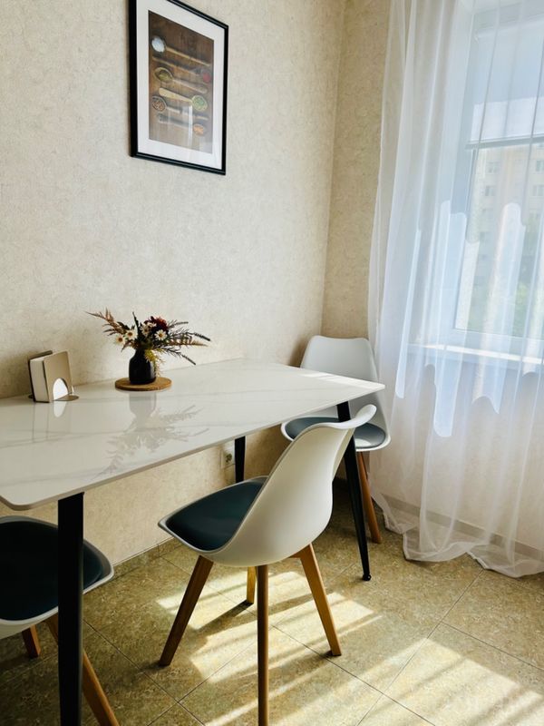 Уголок с прямоугольным столом, четырьмя стульями, вазой с сухоцветами и настенным постером с пряностями.