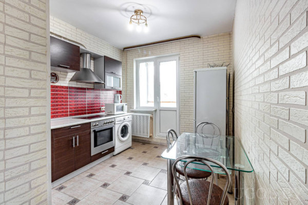 Тёмные шкафы, белая техника, глянцевая плитка, стеклянный стол и окно с дверью на балкон.