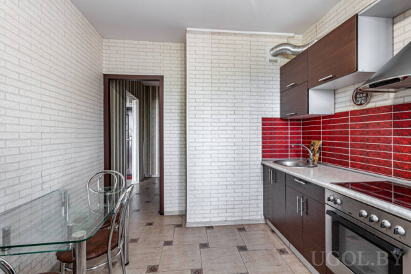 Тёмные фасады, красный фартук, стеклянный стол с металлическими стульями и проход в комнату с полосатыми обоями.