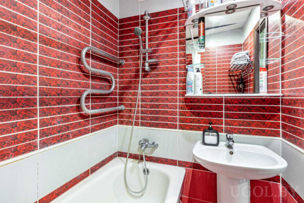 Белая ванна, раковина, зеркало с полками, полотенцесушитель и яркий цветочный узор на плитке.