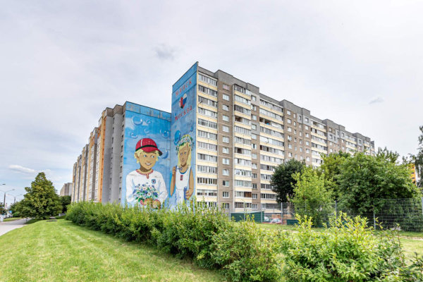 Многоэтажка с рисунком мальчика и девочки, зелёный двор, деревья, кусты и надпись о любви к городу.