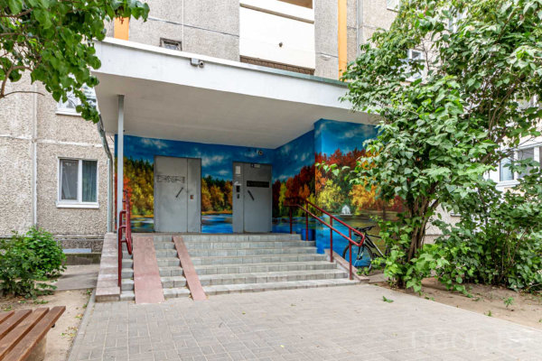 Лестница с красными перилами, две двери, настенная роспись с озером и деревьями, лавочка и кусты у входа.