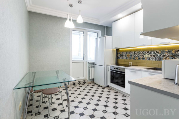 Белые шкафы, плитка с орнаментом, стеклянный стол, два табурета и дверь на балкон с подвесными светильниками.