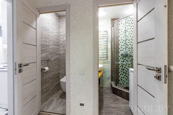 Два открытых помещения: туалет с серой плиткой и душевая с зелёной мозаикой, белая раковина и жёлтая столешница.