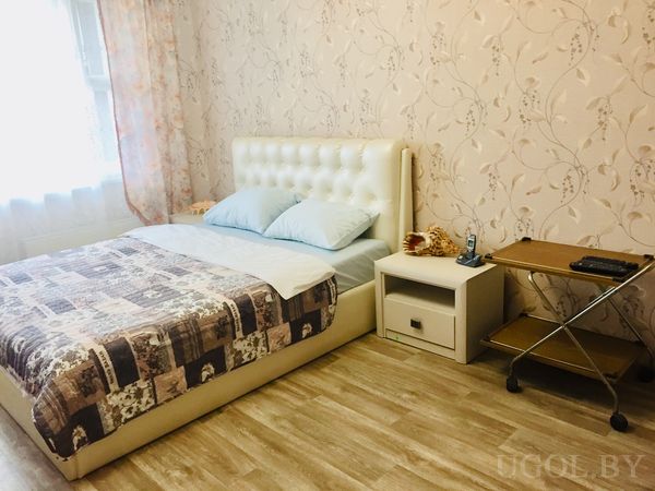 Комната с белой мягкой кроватью, голубыми подушками и лоскутным покрывалом.