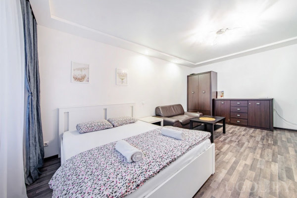 Комната с кроватью, диваном, двумя столиками, шкафом, комодом и серым ламинатом.