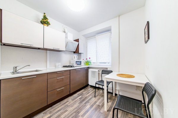 Интерьер с плитой, микроволновкой, столом, чёрными стульями, растением и ёлкой на шкафу.