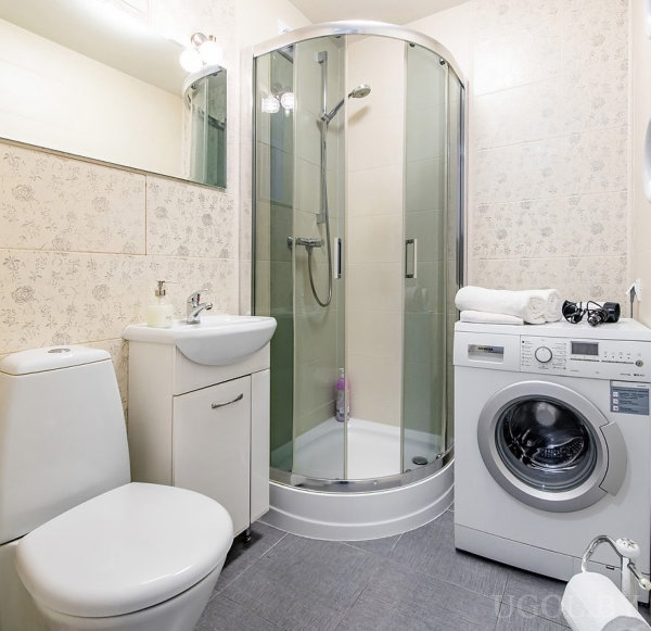 Комната с душевой, унитазом, умывальником, машиной, зеркалом и плиткой с цветочным узором.