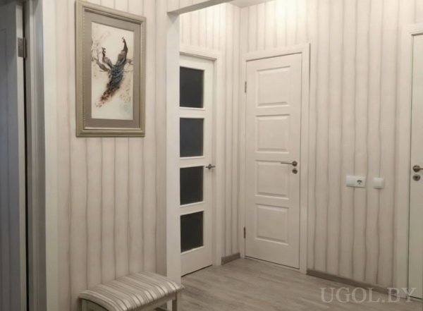 Светлый коридор с вертикальными обоями, белыми дверями, картиной на стене и мягкой скамьёй со striped‑сиденьем.