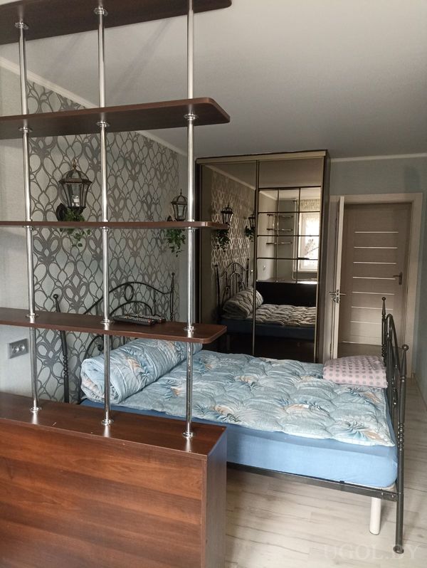 Интерьер с кроватью на металлическом каркасе, перегородкой из полок, зеркальным шкафом и настенными светильниками.
