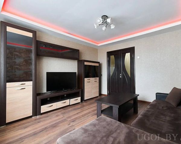 Современная гостиная с диваном, телевизором, красной потолочной подсветкой и дверью с изогнутым стеклом.